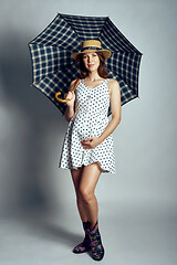 Image showing Pregnant woman in country style summer dress and straw hat standing under umbrella