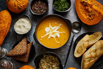 Image showing Delicious pumpkin soup with cream, seeds, bread and fresh herbs 