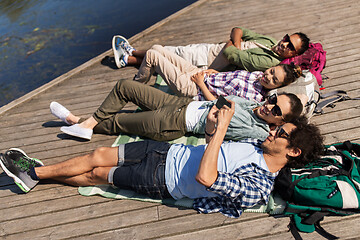 Image showing friends with smartphone lying on lake pier