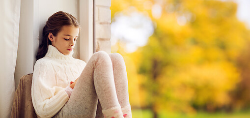 Image showing sad girl sitting on sill at home window in autumn