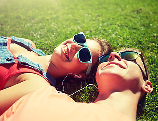 Image showing happy teenage couple with earphones lying on grass