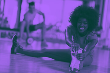 Image showing woman in a gym stretching and warming up man in background worki