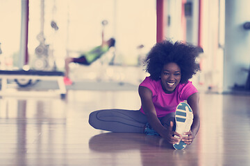 Image showing woman in a gym stretching and warming up man in background worki