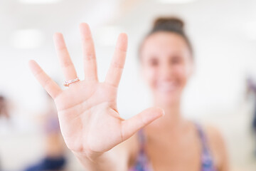 Image showing Fit sporty active woman smiling, wearing fashion sportswear showing an open palm to the camera in yoga studio. Active urban lifestyle.