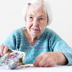 Image showing Concerned elderly woman sitting at the table counting money in her wallet.