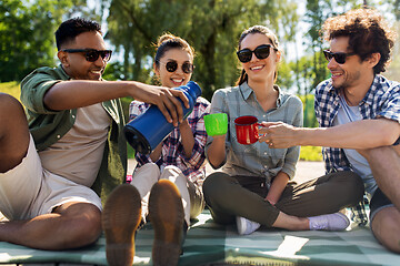 Image showing happy friends drinking tea from thermos in summer