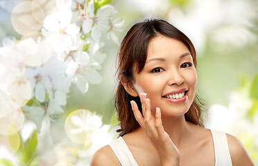 Image showing young asian woman applying moisturizer to her face
