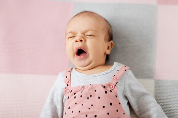 Image showing yawning baby girl in pink suit lying on blanket