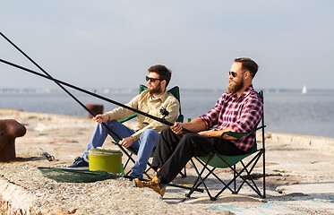 Image showing male friends with fishing rods on sea pier