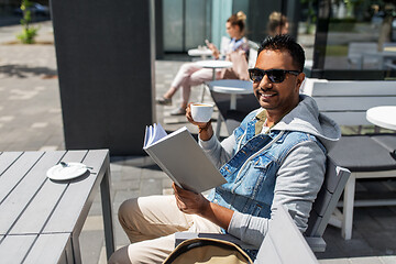 Image showing man reading book and drinking coffee at city cafe