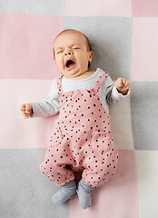 Image showing yawning baby girl in pink suit lying on blanket