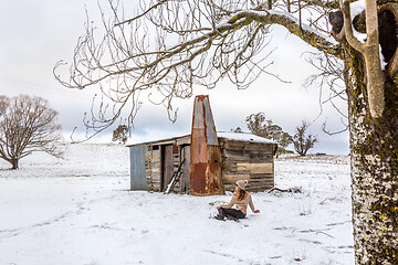 Image showing Woman relaxing in snowy field with old rustic barn