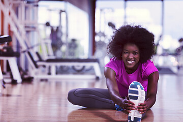 Image showing woman in a gym stretching and warming up man in background worki