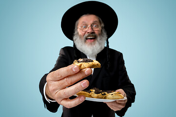 Image showing The senior orthodox Jewish man with black hat with Hamantaschen cookies for Jewish festival of Purim