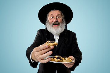 Image showing The senior orthodox Jewish man with black hat with Hamantaschen cookies for Jewish festival of Purim