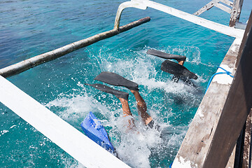 Image showing Scuba divers doing back flip into blue transparent sea from a boat\'s board. There are several ways to get off the boat when diving. One of them is by back roll