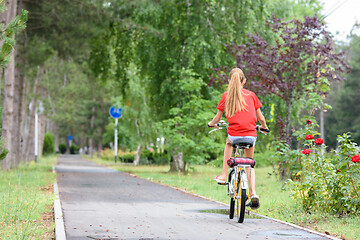 Image showing Girl in a red T-shirt rides on a bike path in the park