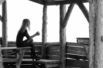 Image showing A girl sits in a wooden arbor on a foggy day and looks into the distance