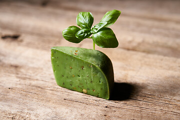 Image showing A piece of gourmet basil cheese with twig of basil on rough wooden planks