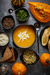 Image showing Delicious pumpkin soup with cream, seeds, bread and fresh herbs in elegant ceramic black bowl