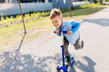 Image showing happy little boy riding scooter in city