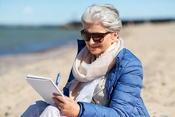 Image showing senior woman writing to notebook on summer beach