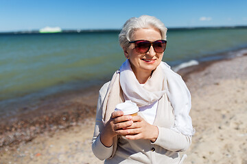 Image showing senior woman drinking takeaway coffee on beach