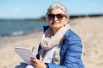 Image showing senior woman writing to notebook on summer beach