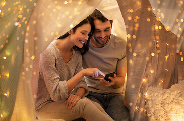 Image showing happy couple with smartphone in kids tent at home