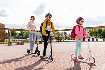 Image showing happy school children with mother riding scooters