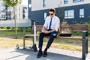 Image showing smiling businessman writing to notebook in city