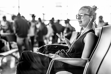 Image showing Female traveler talking on cell phone while waiting to board a plane at departure gates at asian airport terminal.