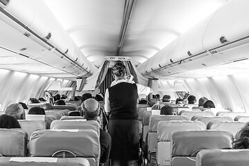 Image showing Interior of commercial airplane with stewardess serving passengers on seats during flight.