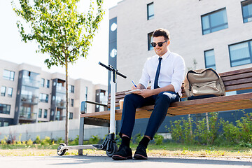 Image showing smiling businessman writing to notebook in city