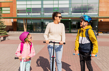 Image showing happy school children with mother riding scooters