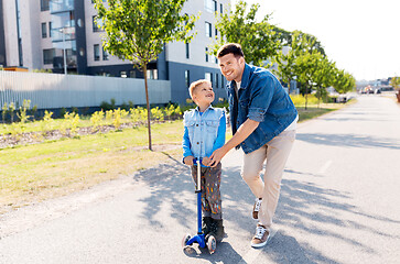 Image showing happy father and little son riding scooter in city