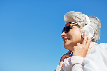 Image showing old woman in headphones listens to music outdoors