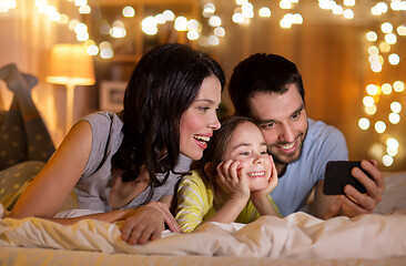 Image showing happy family with smartphone in bed at night