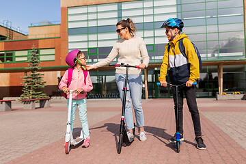 Image showing happy school children with mother riding scooters