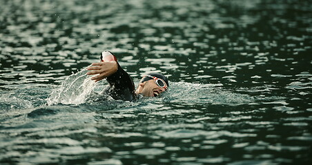 Image showing triathlon athlete swimming on lake in sunrise wearing wetsuit