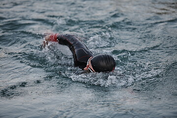 Image showing triathlon athlete swimming on lake in sunrise wearing wetsuit