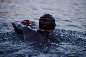 Image showing triathlon athlete swimming on lake in sunrise wearing wetsuit