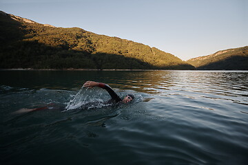 Image showing triathlon athlete swimming on lake in sunrise wearing wetsuit