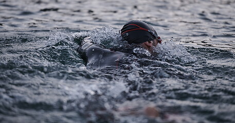 Image showing triathlon athlete swimming on lake in sunrise wearing wetsuit