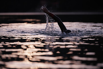 Image showing triathlon athlete swimming on lake in sunrise wearing wetsuit