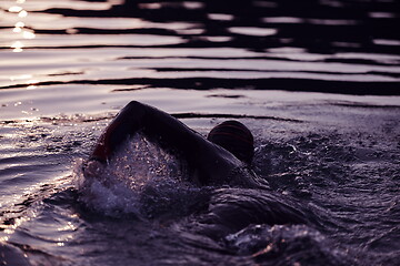 Image showing triathlon athlete swimming on lake in sunrise wearing wetsuit