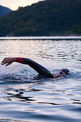 Image showing triathlon athlete swimming on lake in sunrise wearing wetsuit