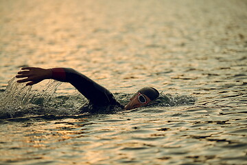 Image showing triathlon athlete swimming on lake in sunrise wearing wetsuit