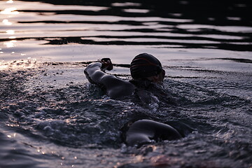 Image showing triathlon athlete swimming on lake in sunrise wearing wetsuit