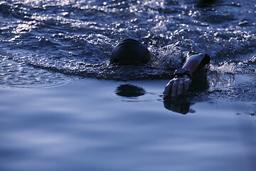 Image showing triathlon athlete swimming on lake in sunrise wearing wetsuit